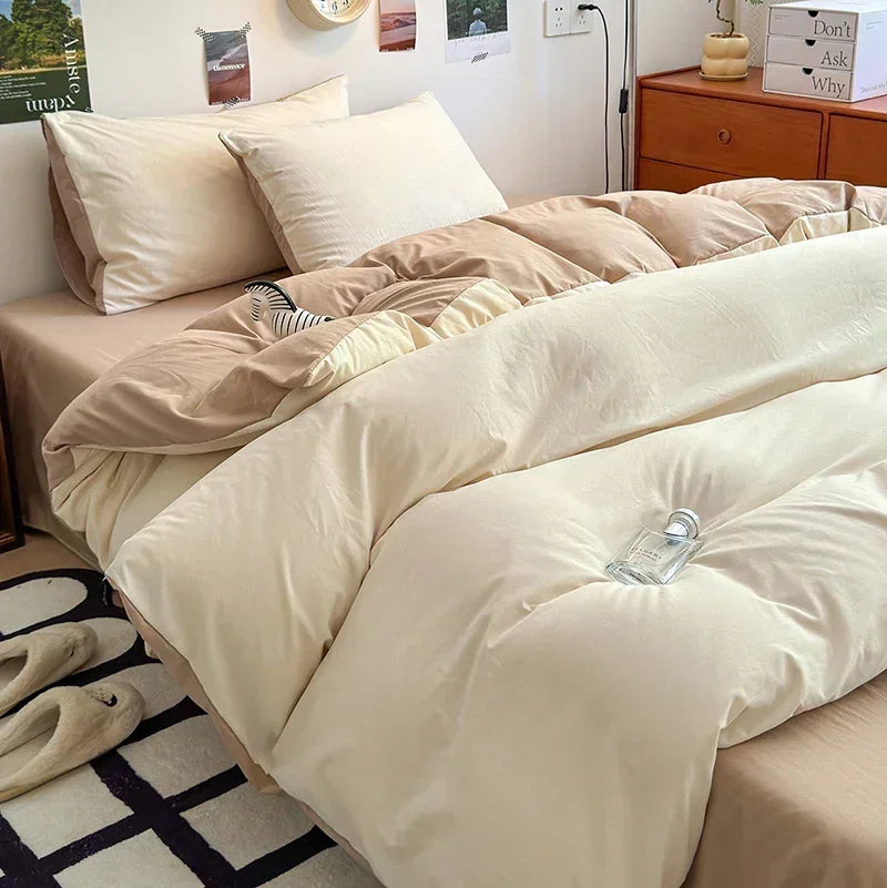 Beige comforter on a bed in a bedroom setting with slippers and a rug.