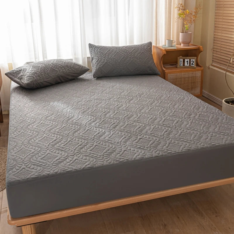 Gray quilted mattress cover on a bed in a bedroom setting.