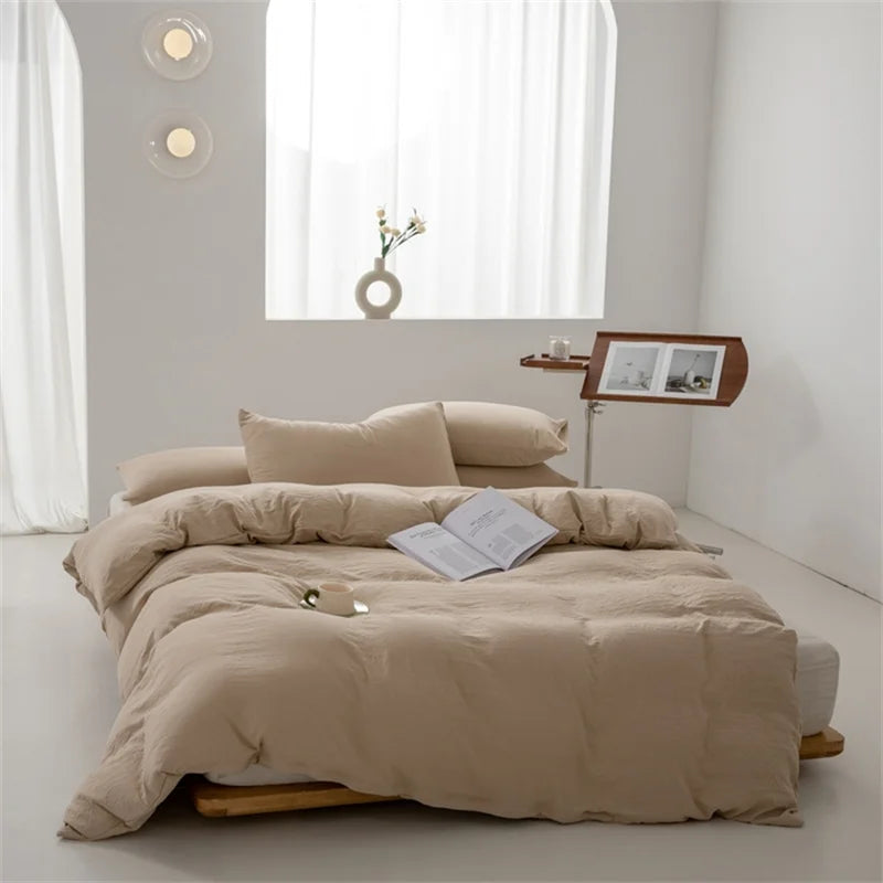 Beige bedding set on a bed in a minimalistic room with a window and side table.