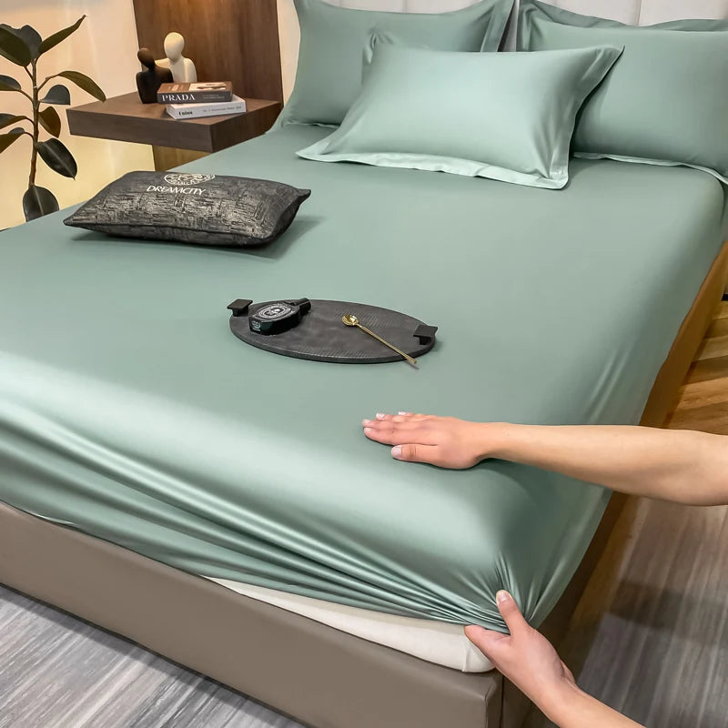 Person adjusting a green satin sheet on a bed with decorative items.