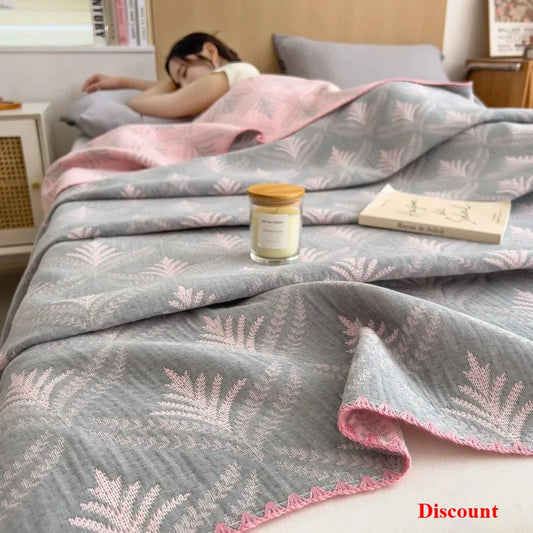 Person lying in bed under a gray and pink patterned blanket with a candle and book on the bed.