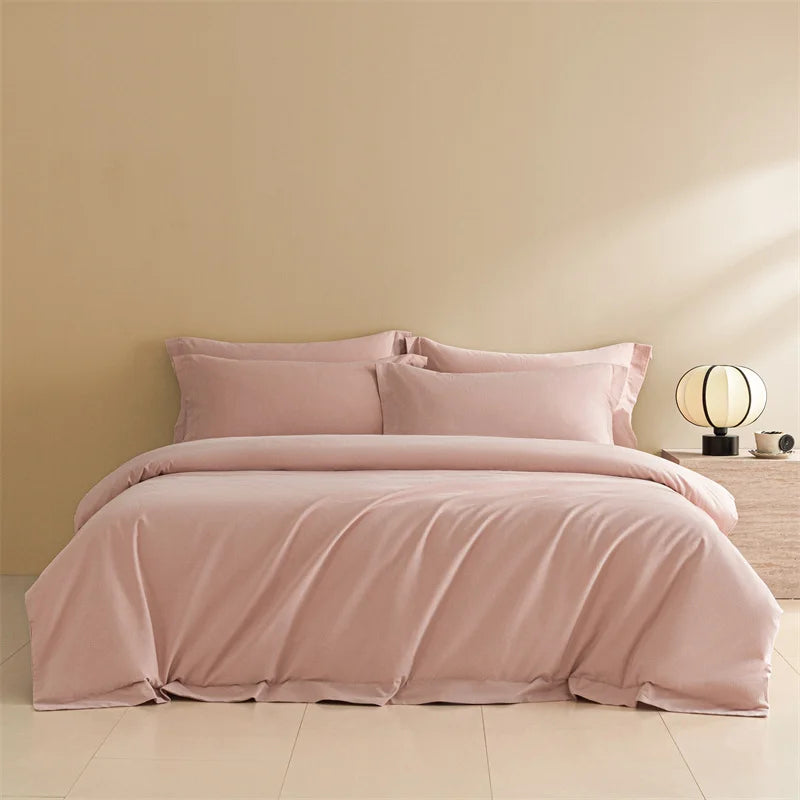 Pink bedding set on a bed against a beige wall with a lamp and nightstand.