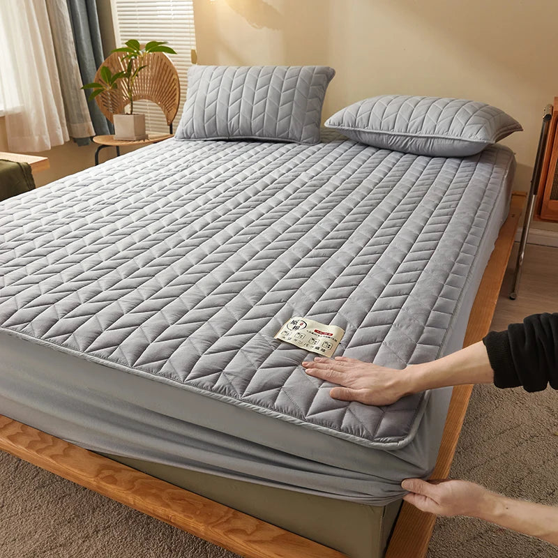 Person adjusting a gray quilted mattress cover on a bed in a bedroom.
