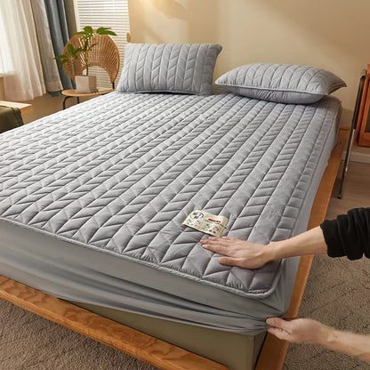 Person adjusting a gray quilted mattress cover on a bed in a bedroom.