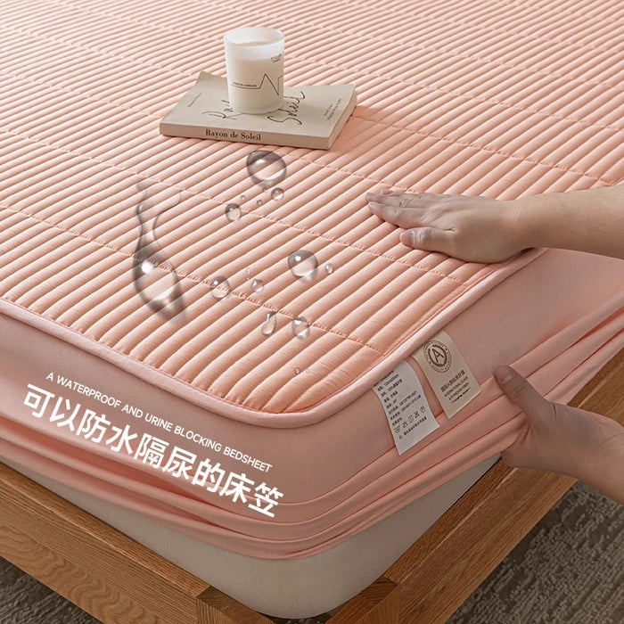Pink waterproof bedsheet being stretched over a mattress with a hand holding it, on a wooden floor.