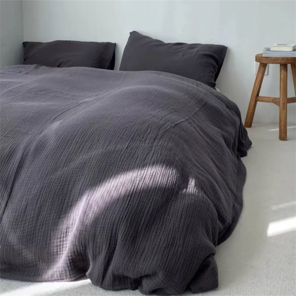 Dark gray bedding set on a bed with a wooden stool in the corner.