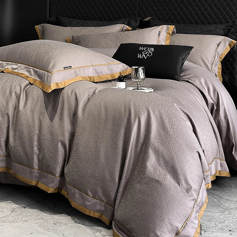 Gray textured bedspread with gold trim on a bed, featuring a visible brand logo.