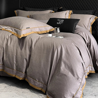 Gray textured bedspread with gold trim on a bed, featuring a visible brand logo.