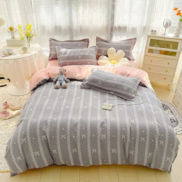 Gray and pink bedding set with decorative pillows and a teddy bear on a bed in a bright room.