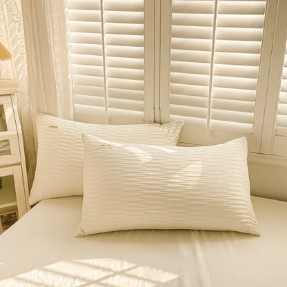 Two white pillows on a bed with light-colored walls and window blinds in the background.