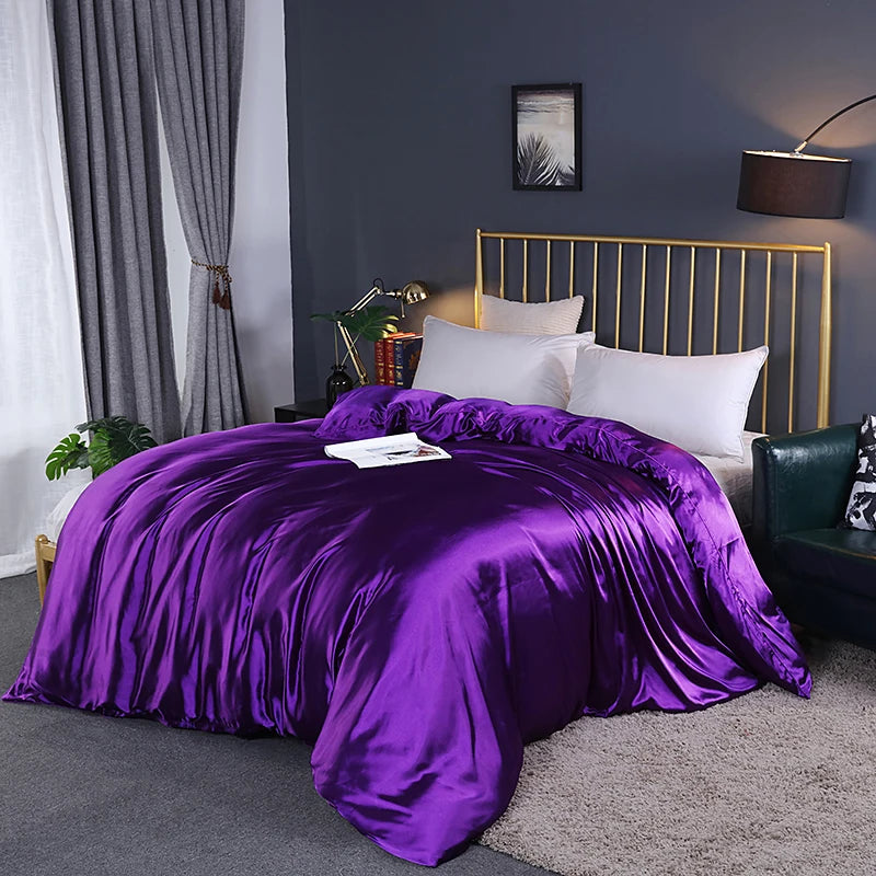 Purple comforter on a bed in a bedroom with a gold headboard and gray walls.