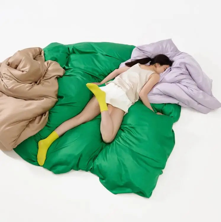 Person lying on a large green bean bag with colorful blankets.