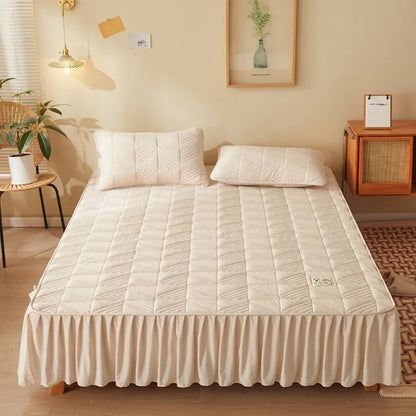 Beige mattress cover on a bed in a room with a lamp, plant, and side table.