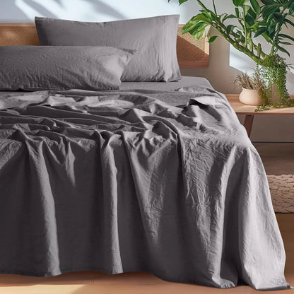 Gray bedding set on a bed with a wooden headboard and plants in the background.