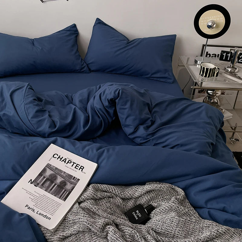 Blue bedding set on a bed with a magazine and sweater in the foreground.