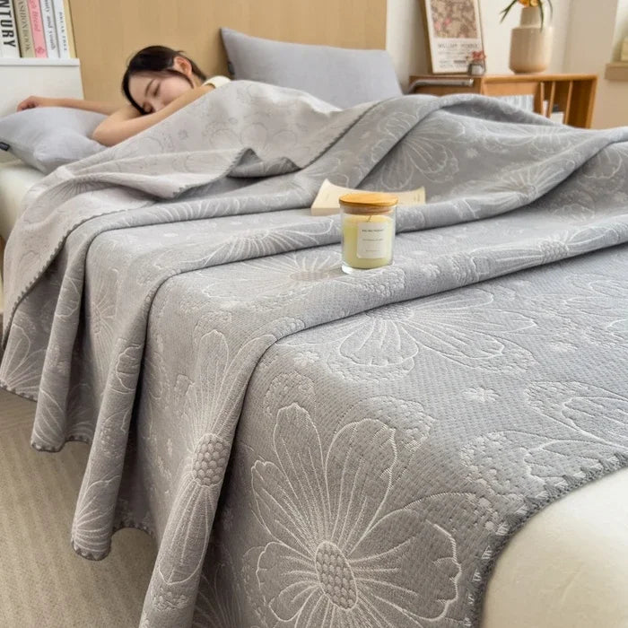Woman sleeping under a floral-patterned gray blanket with a candle on the bed.