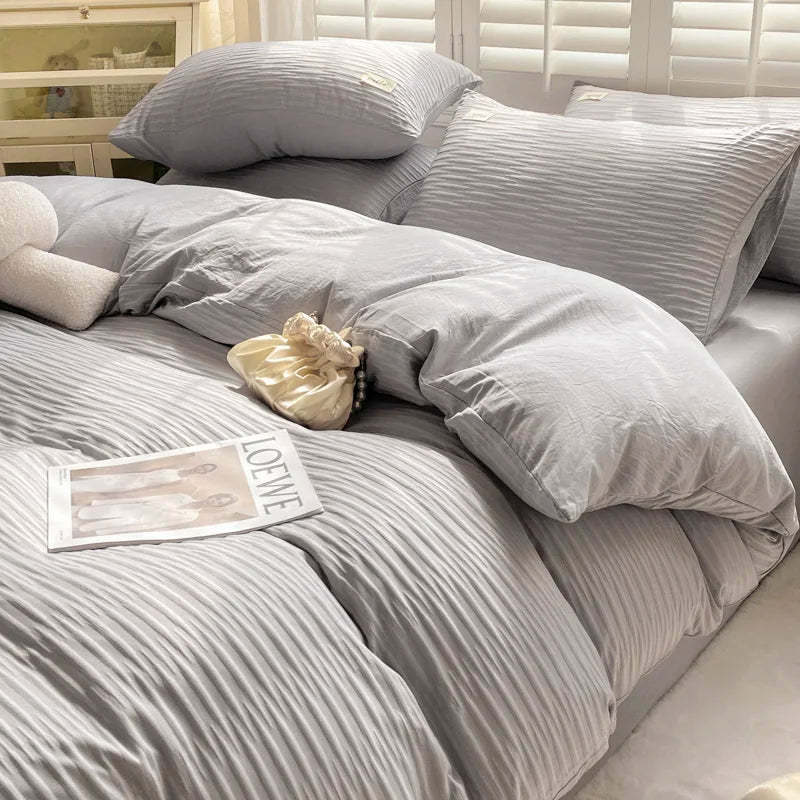 Gray striped bedding set on a bed with pillows and a small pillow on a shelf.