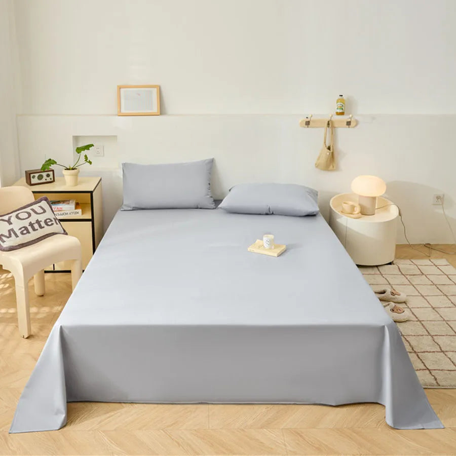 Bed with gray fitted sheet and pillows in a bedroom setting