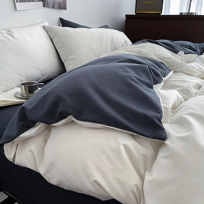 Bed with white bedding and a gray blanket, featuring a cup and saucer on a nightstand.