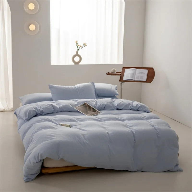 Blue bedding set on a bed in a bright bedroom with a window and small table.
