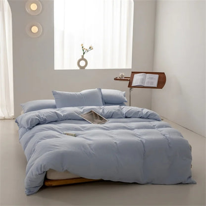 Blue bedding set on a bed in a bright bedroom with a window and small table.