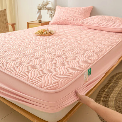 Pink quilted mattress cover being placed on a bed in a bedroom setting.