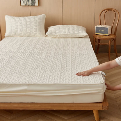 Person adjusting a mattress cover on a bed with pillows and a chair in the background.