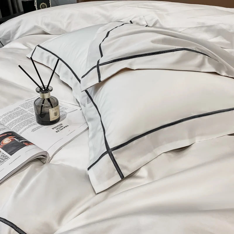 White bedding set with black piping on a bed, featuring a diffuser and magazine.
