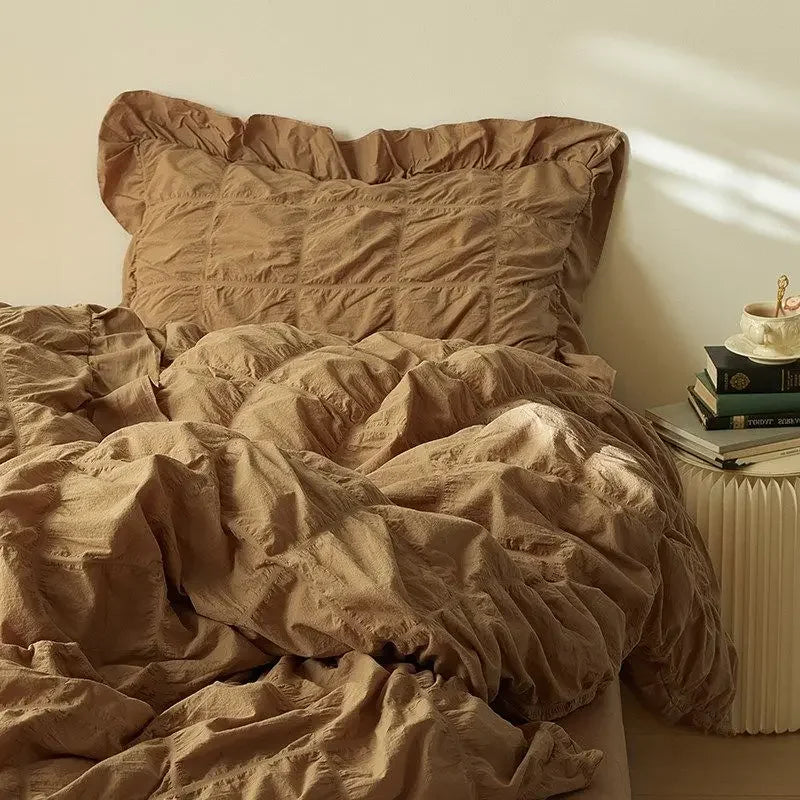 Brown textured bedding set on a bed with a pillow and books on a nightstand.