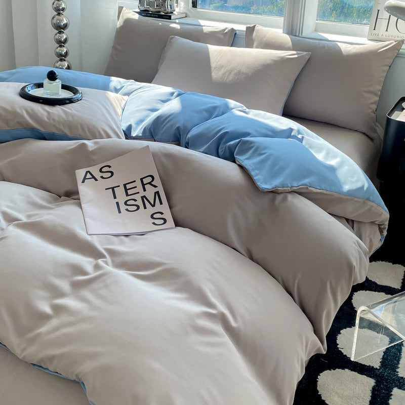 Neatly made bed with gray and blue bedding, featuring a pillow with text.