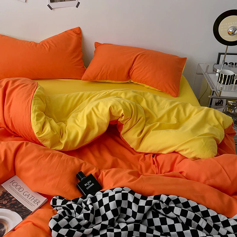 Orange and yellow bedding with a black and white checkered blanket on a bed.