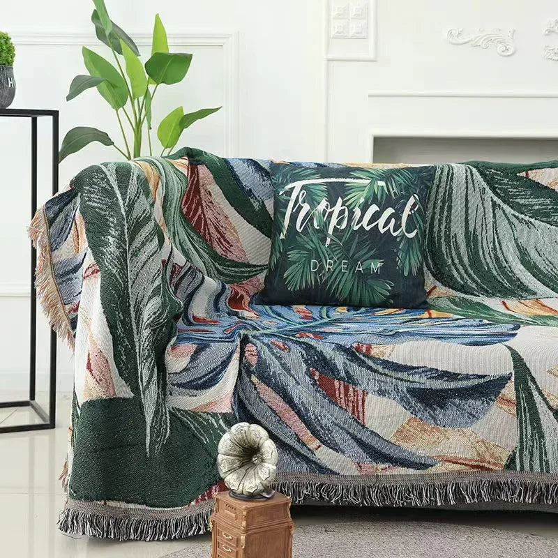 Tropical leaf patterned throw blanket draped over a sofa with a decorative pillow.