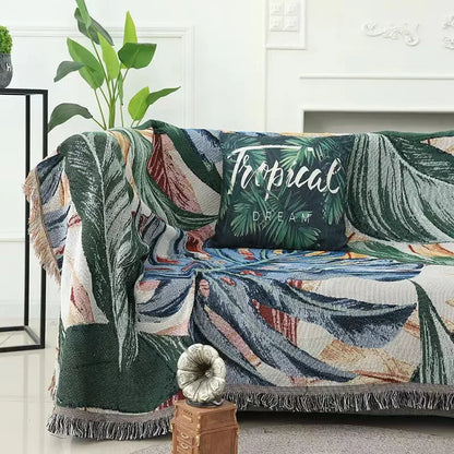 Tropical leaf patterned throw blanket draped over a sofa with a decorative pillow.