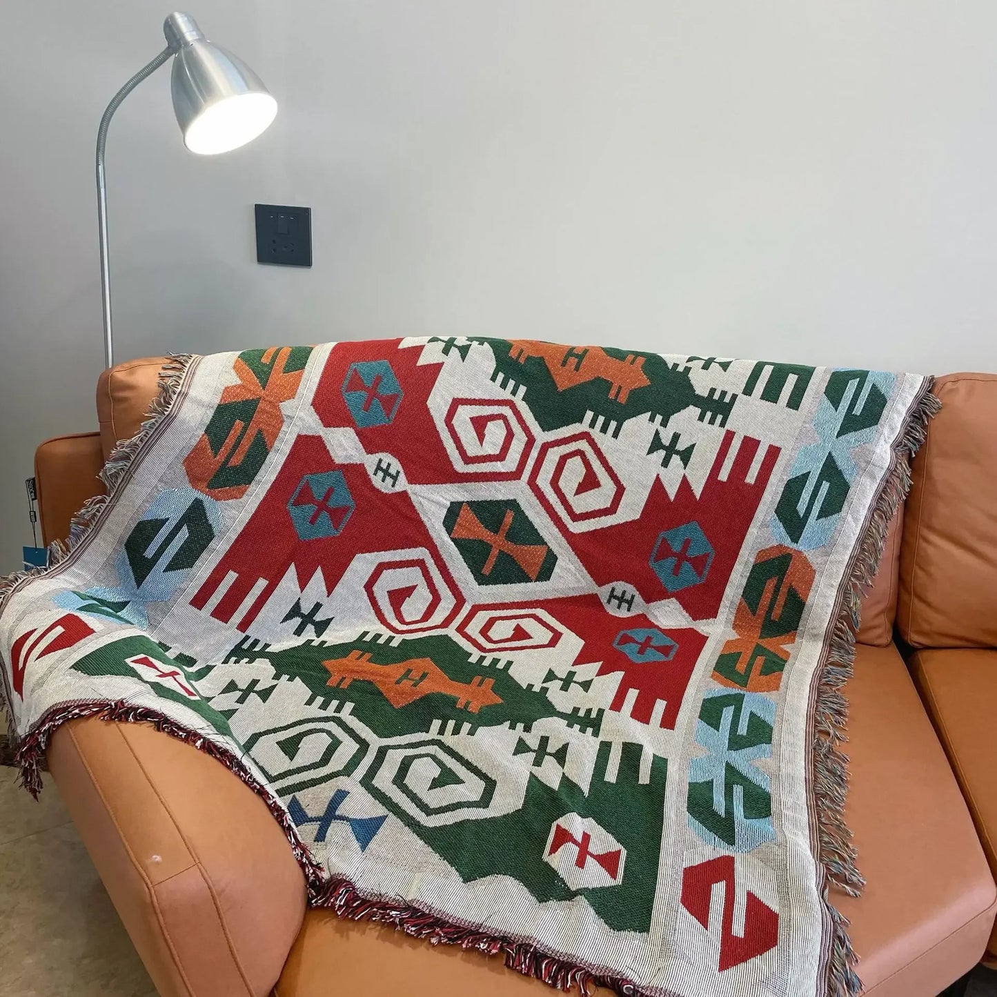Colorful geometric patterned blanket draped over a brown sofa with a lamp in the background.