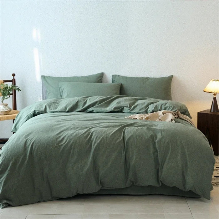 Green bedding set on a bed in a bedroom with a lamp and plant.