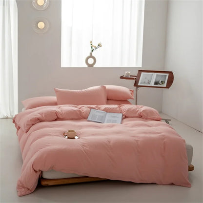Pink bedspread set on a bed in a minimalistic room with a window and side table.