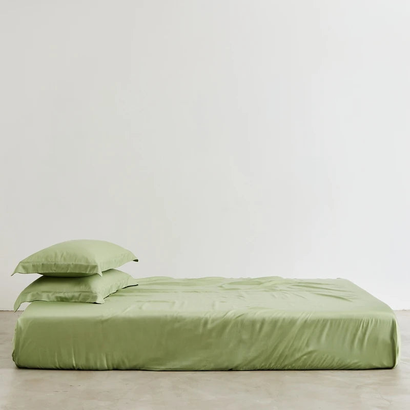 Green bed sheets and pillowcase set on a bed against a white wall.
