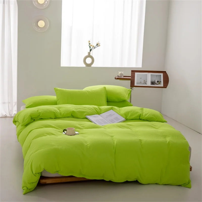 Green bedspread set on a bed in a bright room with a window and small table.