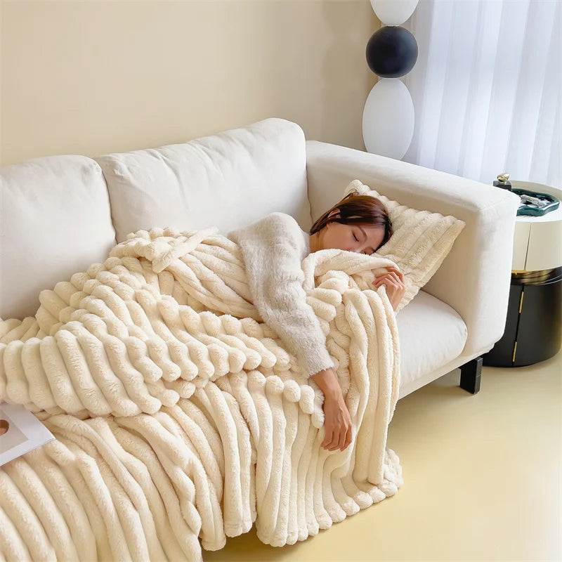 Person lying on a white couch under a fluffy beige blanket in a cozy living room.