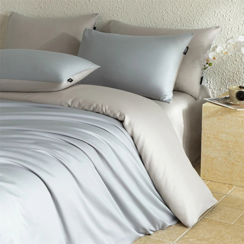 Neatly made bed with light gray bedding and pillows in a bedroom setting.