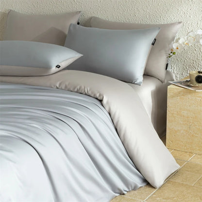 Neatly made bed with light gray bedding and pillows in a bedroom setting.