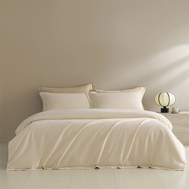 Beige bedding set on a bed in a minimalistic room with a lamp and nightstand.