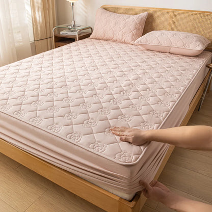 Person adjusting a quilted mattress cover on a bed in a bedroom.