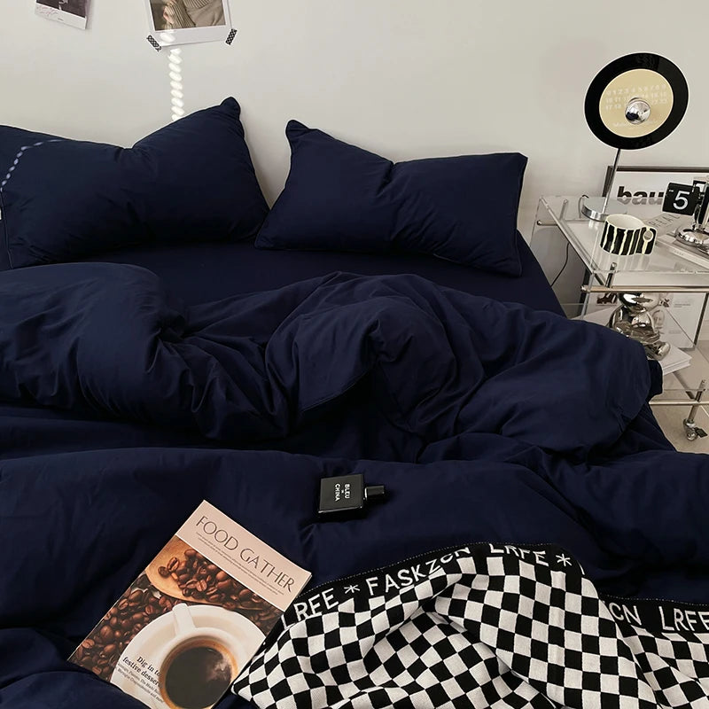 Navy blue bedding set with a book and remote control on a bed in a bedroom.
