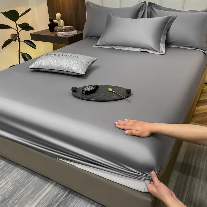 Person adjusting gray satin sheet on a bed with decorative items.