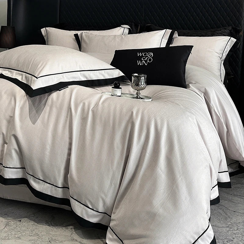 White bedspread with black trim on a bed, featuring a black pillow with 'WOW' text.