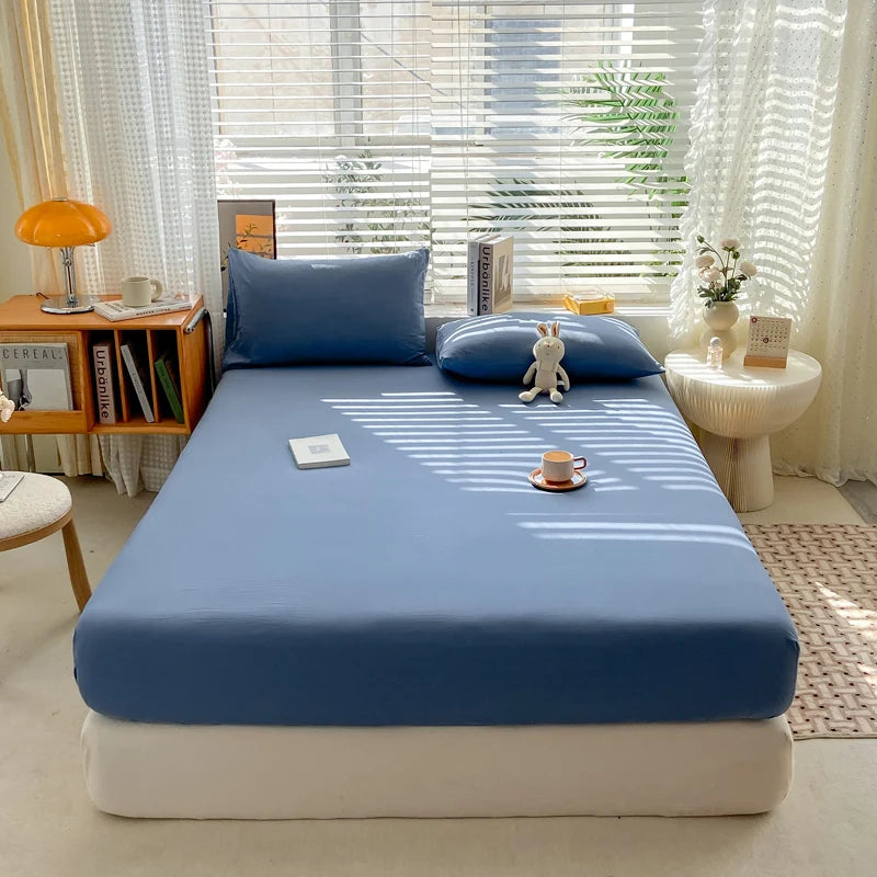 Blue bedspread on a bed in a bright room with window blinds and decor.
