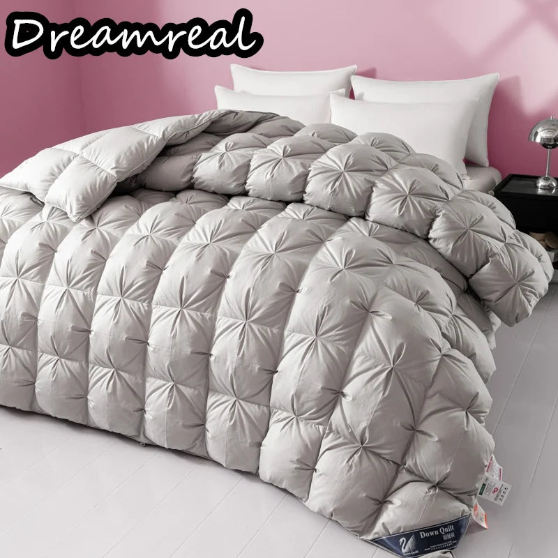Gray quilted comforter on a bed with white pillows against a pink wall, featuring the brand 'Dreamreal'.