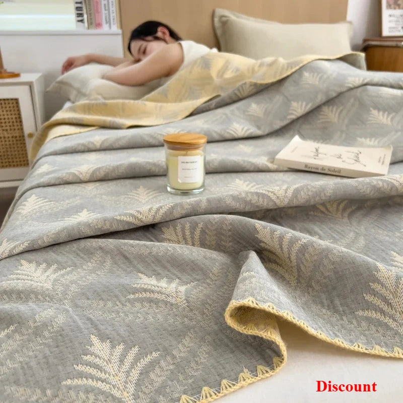 Person sleeping under a patterned blanket with a candle and box on a bed.